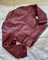 Campera corta de cuero sintético color borgoña, con cuello solapa, corte oversize, cierre cruzado con hebillas y cinturón.