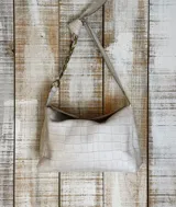 Cartera tipo bolso de mano color beige con textura símil piel de cocodrilo. Tiene correa corta de hombro con eslabones dorados.