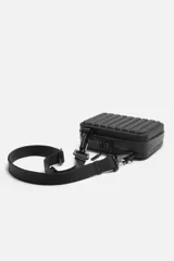Bandolera rígida negra con acabado engomado y relieve. Tiene un compartimento principal con doble cremallera, un bolsillo interior de rejilla y asa de hombro ajustable y extraíble.