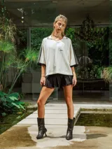 Chomba de tejido de punto cerrado color blanco, con cuello polo y mangas cortas. Presenta un bordado sutil en el frente y tres franjas negras en los hombros.