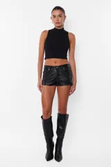 Short negro de cuerina, tiro medio, con bolsillos laterales y traseros, presillas en la cintura y botón metálico.