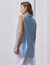 Camisa sin mangas color celeste, confeccionada en lino. Presenta cuello camisero, escote en V, abertura frontal con botones, dos bolsillos de parche en el pecho y terminación con botones en los laterales.