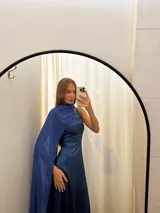 Vestido largo de tafeta con brillo, color gris o plateado, con escote asimétrico de un solo hombro y una pieza de seda liviana que cae como una capa o chal.