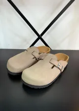 Zuecos beige con hebilla metálica ajustable, plantilla de corcho y suela de goma negra.