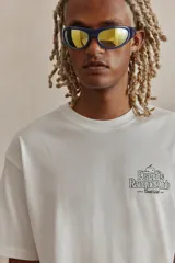 Remera blanca de corte holgado con cuello redondo y estampado de Snoopy con la leyenda "Peanuts Racquet Club" en el pecho.