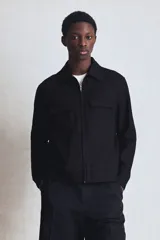 Campera camisera negra de corte recto, con cuello clásico, cierre frontal con cremallera, dos bolsillos de parche con solapa en el pecho y bolsillos laterales.