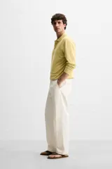 Pantalón chino color crema de corte recto, confeccionado en tejido de algodón con elasticidad. Cuenta con bolsillos frontales y traseros de plastrón con botón. Cierre frontal con cremallera y botón.