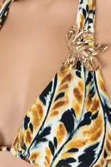Top de bikini con estampado abstracto en tonos amarillo mostaza, negro y blanco. Diseño de cuello halter con tiras ajustables y detalle metálico dorado con forma de hoja en la unión de las copas.