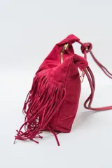 Bolso de hombro tipo hobo color rojo oscuro, confeccionado en material tipo gamuza o nobuk, con flecos largos en la parte inferior. La correa es delgada y se anuda en la parte superior.
