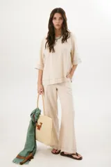 Blusa de lino color beige claro, con mangas 3/4 y cuello redondo. Presenta pespuntes a contratono en el centro, puños y ruedo.