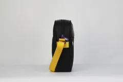 Morral cruzado de nylon negro con textura de rombos, con el logo de Los Angeles Lakers en tonos morado y dorado, y el logo de la NBA en blanco en la parte inferior. Posee correa regulable de color amarillo.