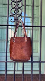 Bolso tipo tote de cuero con pelo color marrón y blanco, con manijas de cuero crudo.