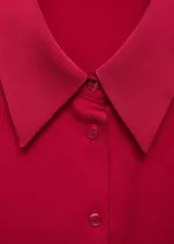 Camisa color crema de tejido fluido con textura y acabado satinado. Tiene cuello clásico, cierre de botones frontal y mangas largas con puños abotonados.