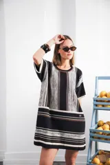 Vestido corto tejido color crudo con rayas verticales marrones y celestes. Tiene cuello redondo y mangas cortas con terminaciones en color rojo.