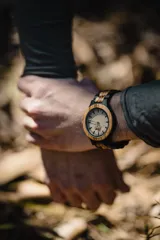 Reloj de pulsera con caja y esfera de madera clara, malla de madera oscura con incrustaciones de madera clara.