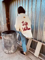 Sweater tejido en lana color crudo, con cuello alto, corte holgado y bordado a mano en color rojo con la frase "Life Walker" en la espalda.