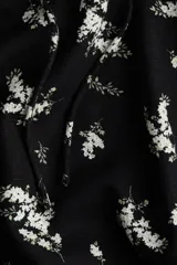 Vestido largo negro con estampado floral blanco, de tejido liviano de mezcla de lino y viscosa. Modelo con mangas cortas abullonadas, escote corazón con tiras finas y copas preformadas con frunces. Elástico fino en escote, hombros, mangas y cintura. Cierre lateral oculta y bajo recto con tajo pronunciado en un lado.