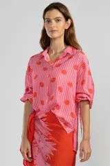 Camisa de manga larga color rosa con rayas verticales rojas y estampado de flores rojas. Tiene cuello camisero, puños elastizados y lazos regulables en los costados del ruedo.