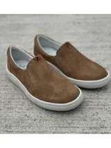 Zapato slip-on color marrón con capellada de cuero sintético microperforado, elástico lateral y suela blanca.