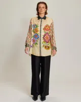 Camisa de manga larga color crema con estampado de flores y detalles geométricos, cuello clásico negro y cierre con botones.