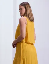 Vestido largo color mostaza de crepe, marca Marissa Olivia. Escote redondo con sobrecapa y detalle de crochet en los hombros. Corte en la cintura con punto smock. Sin mangas.