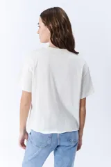 Remera blanca de manga corta con cuello redondo y pinzas laterales que crean un drapeado en la parte delantera.