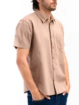 Camisa de manga corta color beige, confeccionada en 100% algodón, con cuello clásico, cierre frontal con botones y bolsillo en el pecho.