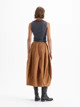 Pollera larga tipo balloon color marrón, confeccionada en popelina asargada. Presenta recortes verticales que aportan volumen y estructura, bolsillos ocultos en los laterales y bordado de logo JCH en el frente.