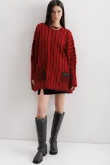 Sweater tejido de punto color fucsia con diseño de trenzas verticales en color naranja. Tiene cuello redondo y dos bolsillos frontales.