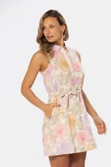 Vestido corto sin mangas de lino con estampado floral en tonos lavanda, rosa y amarillo. Presenta cuello camisero, cierre frontal parcial con botones y cinturón de lazo en la cintura.