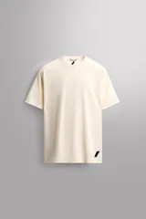 Camiseta deportiva color crema de tejido técnico ligero y elástico con perforaciones. Tiene cuello redondo, manga corta y logo estampado.