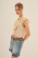 Camisa color crema de corte corto con escote redondo, mangas cortas con volados y jareta ajustable en el ruedo.