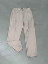 Pantalón de gabardina color beige, corte recto con elástico en la cintura y puños elastizados. Tiene bolsillos laterales con cierre de cremallera.