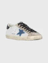 Championes urbanos Golden Goose modelo Super Star, color blanco con detalles en gris, negro y azul. Confeccionados en cuero y gamuza, con efecto desgastado y estrella azul en el lateral.