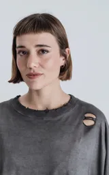 Remera gris de manga corta con calce oversize, con cuello redondo y efecto gastado. Presenta roturas en los hombros y el pecho.