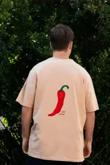 Remera color crema de manga corta con estampado de un ají rojo y la frase "Just Chilli" en la espalda.