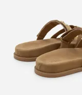 Sandalias planas color marrón claro con efecto gamuza y dos tiras con tachas doradas.