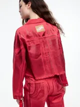 Campera corta de denim color rojo con textura metalizada, cuello camisero, cierre frontal con botones a presión, bolsillos de parche en el pecho y ruedo desflecado.