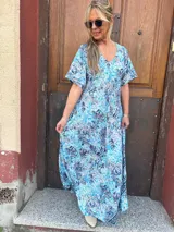 Vestido largo de seda con estampado floral en tonos turquesa, azul y blanco. Tiene escote en V y mangas cortas.
