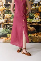 Conjunto de top sin mangas y falda midi color fucsia, con botones dorados. La falda presenta una abertura lateral.