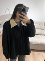 Campera negra de pana con cuello beige, cierre frontal y bolsillos laterales.