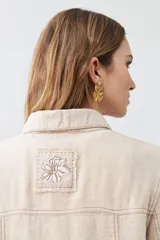 Chaqueta color beige melange de lino con pespuntes a contraste, cuello camisero, cierre frontal con botones, bolsillos de parche en el pecho y corte recto.