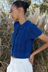 Chaqueta de punto azul con cuello redondo y manga corta. Cierre frontal con botones forrados y diseño en relieve.