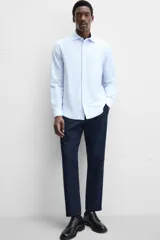 Camisa celeste a rayas verticales blancas, de corte recto, con cuello italiano abierto, manga larga con puños abotonados y cierre frontal con botones.
