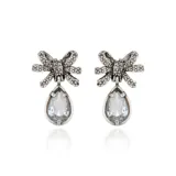 Aros colgantes plateados con forma de moño con incrustaciones de strass y dije de cristal transparente en forma de lágrima.