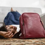 Mochila negra de símil cuero con costuras diagonales en el frente. Tiene un bolsillo frontal con broche magnético, asa de mano y correas regulables.