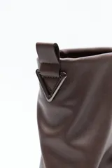 Bota de caña baja negra de poliuretano con acabado liso y efecto fruncido. Presenta puntera redondeada, base baja y cierre trasero con tirador metálico.