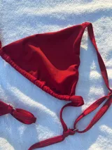Conjunto de bikini rojo brillante, compuesto por un corpiño triangular con tirantes finos y una tanga con tirantes laterales ajustables.