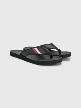 Ojotas negras Tommy Hilfiger con tira ancha de poliuretano acolchada y suela de goma EVA. Detalle de cinta distintiva con los colores de la marca en la tira.