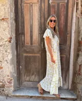 Vestido largo estampado con flores blancas sobre fondo dorado, con mangas cortas con volados y escote en V.